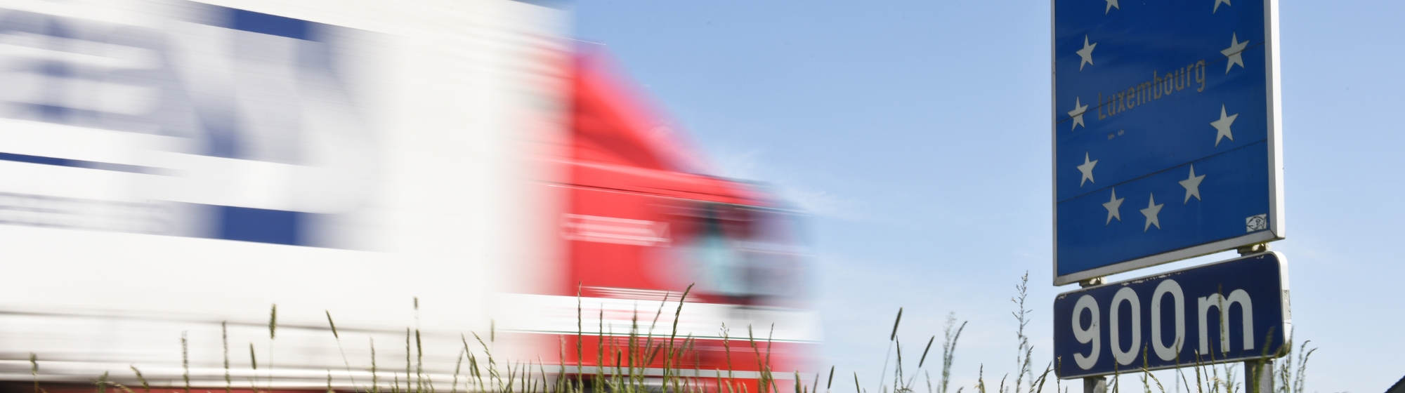 Camion roulant à vive allure devant un panneau européen au Luxembourg avec de l'herbe devant lui