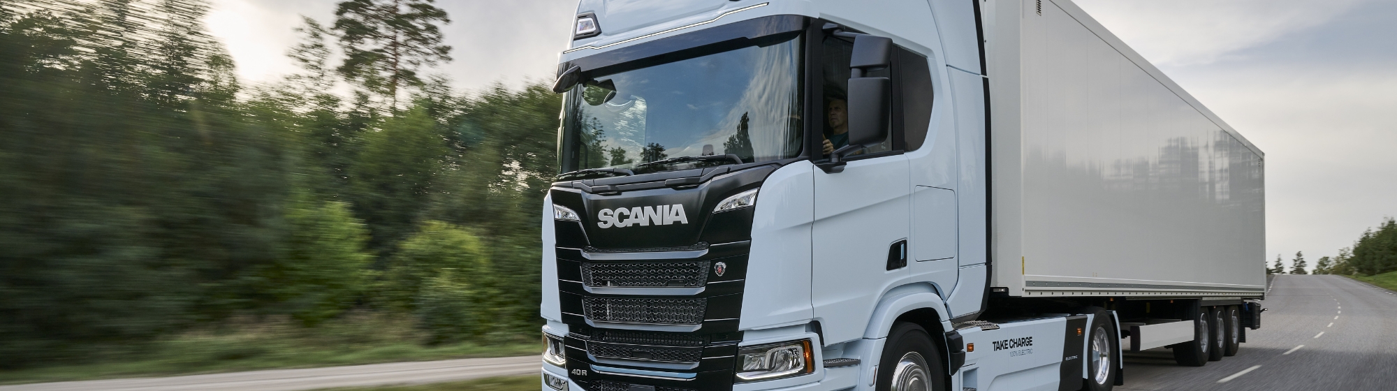 camion blanc scania roulant sur une route avec de la foret