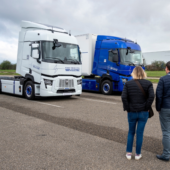 Deux camions électriques Renault Trucks, un blanc et un bleu, observés par deux personnes en extérieur